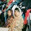 Two women sitting in front of a large pile of clothes